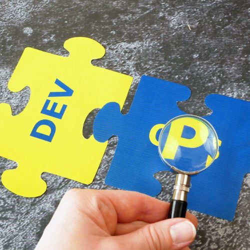 hands with magnifier glass with words Dev and Ops puzzles. Concept for software engineering culture and practice, closeup